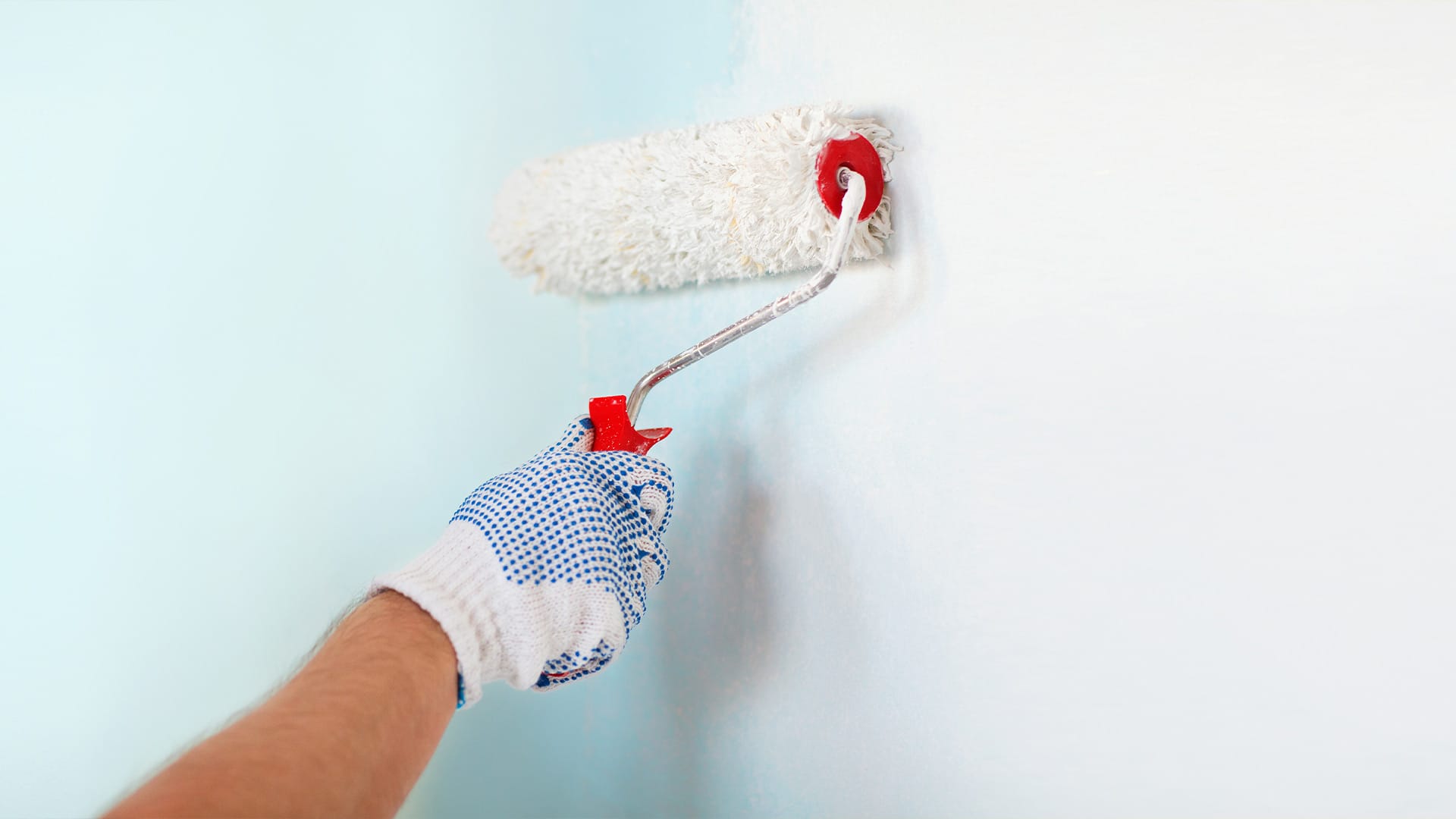 Person painting a wall with a white roller.
