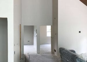 Interior of a room under construction with high ceilings, white walls and protective covering on the furniture.