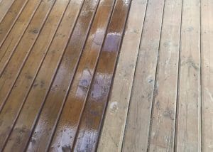 Half of a wooden deck professionally stained and a white cloth rag in the corner.