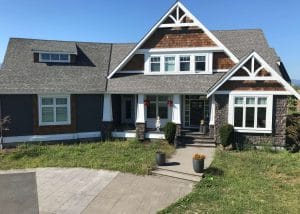 A suburban house with a gray exterior, stone accents, and a front lawn under a clear blue sky, with a mountain in the distance.