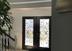 Sunlight filtering through a decorative glass doorway in a bright entryway with a staircase to the left.
